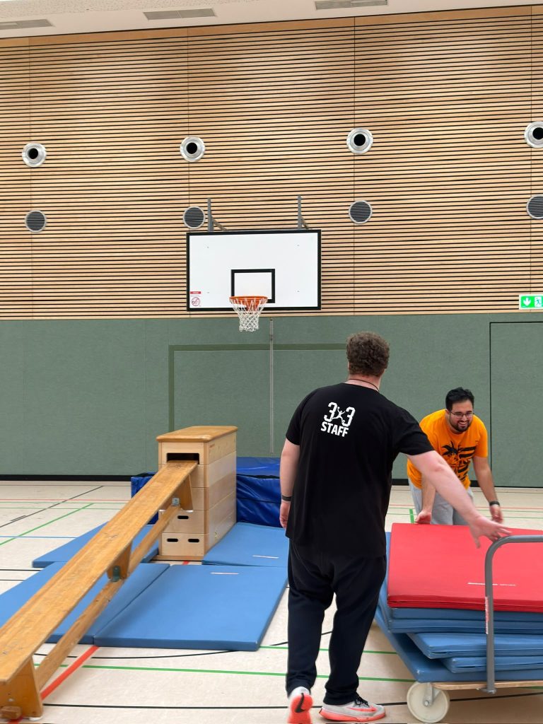 Zwei Coaches bauen den Parcours aus Bank, Kasten und Matten auf